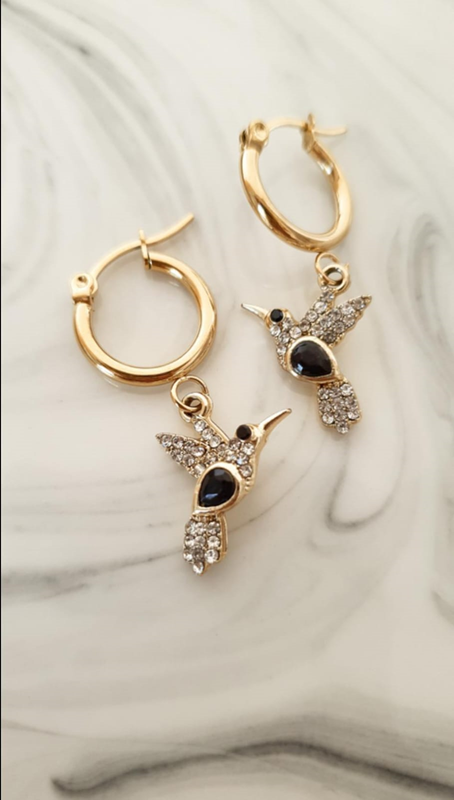 Argollas Colibrí - Acero Dorado1 Argollas Colibrí en Acero Dorado, con detalles en cristal, puntos de luz y piedritas negras.